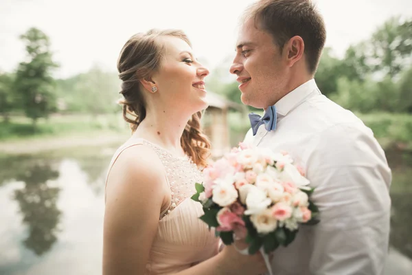 Щаслива весільна пара обіймає і посміхається один одному на фоні озера, лісу — стокове фото