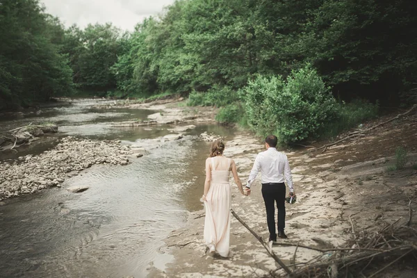 Elegante gentile sposo elegante e sposa vicino al fiume con pietre. Matrimonio coppia innamorata — Foto Stock