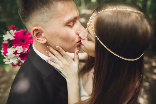 Hermosa joven pareja de boda se besa y sonríe en el parque — Foto de Stock