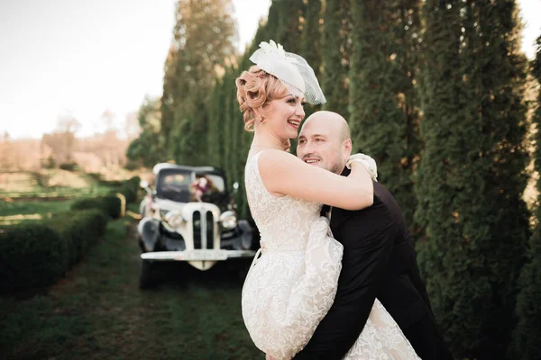 Feliz pareja recién casada, el hombre y la esposa besándose cerca de coche retro con estilo — Foto de Stock