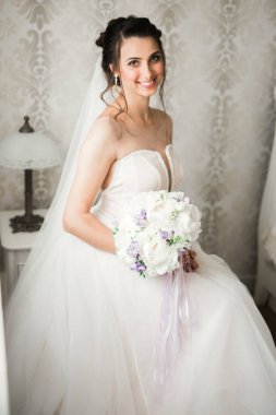 Cüppeli muhteşem gelin bir odada düğün töreni için poz veriyor ve hazırlanıyor.