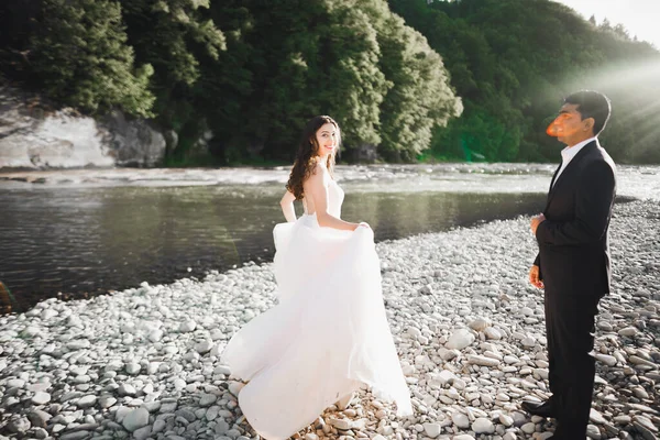 Elegante novia rubia feliz y elegante novio en el fondo de un hermoso río en las montañas —  Fotos de Stock