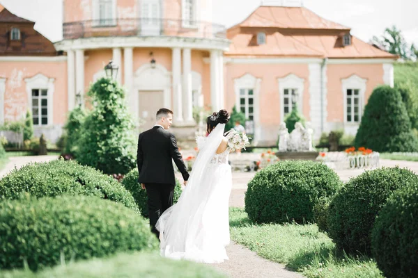 結婚式の日に公園を歩く幸せな新婚旅行のスタイリッシュなカップル花束 — ストック写真