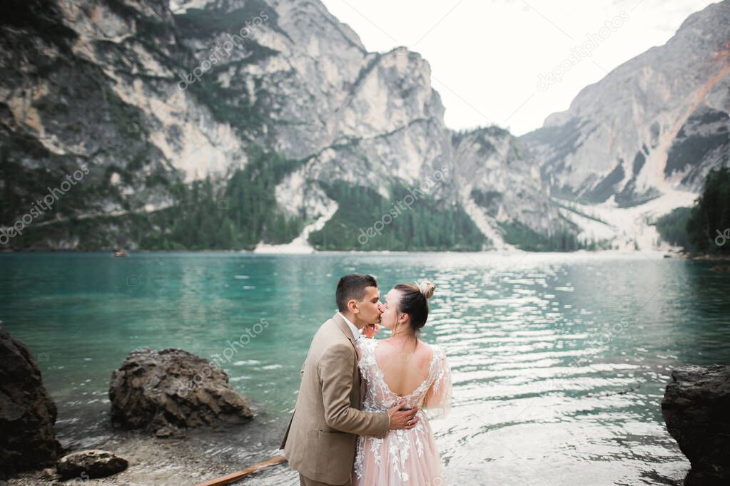 Wedding couple on the nature is hugging each other near a beautiful lake in the mountains.. Beautiful model girl in white dress. Man in suit