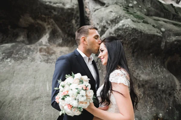 Schönes junges Hochzeitspaar posiert mit Blumenstrauß in den Händen — Stockfoto