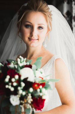 Zarif beyaz elbiseli güzel gelin elinde bir buket çiçek tutuyor.