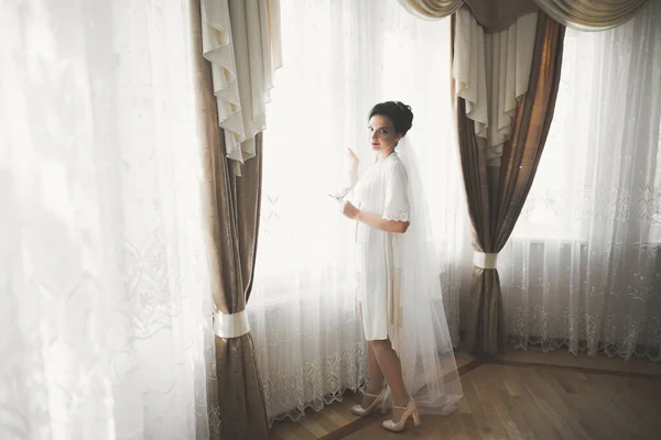 Splendida sposa in accappatoio in posa e preparazione per la cerimonia di nozze faccia in una stanza — Foto Stock