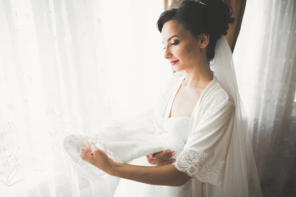 Prachtige bruid in badjas poseren en voor te bereiden op de bruiloft ceremonie gezicht in een kamer — Stockfoto