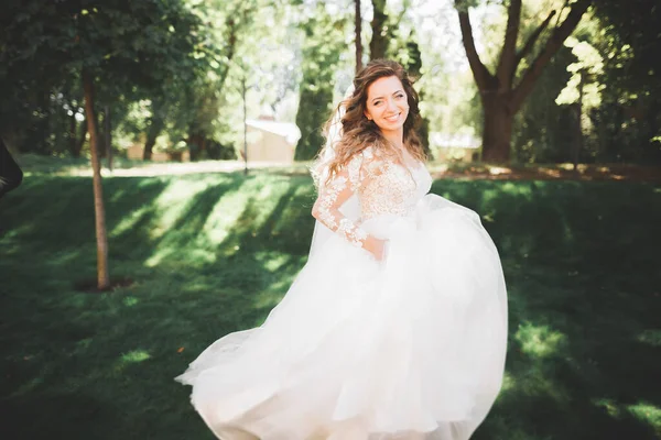 Schöne Braut im eleganten weißen Kleid mit Blumenstrauß posiert im Park — Stockfoto