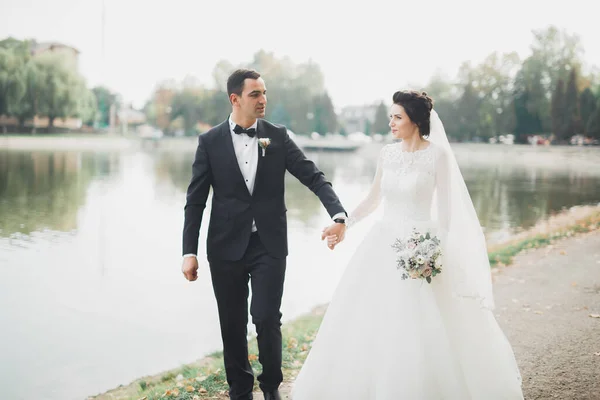 Stijlvol paar gelukkige pasgetrouwden wandelen in het park op hun trouwdag met boeket — Stockfoto