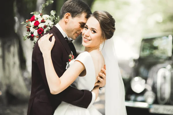 Feliz casal recém-casado, homem e mulher beijando perto de carro retro elegante — Fotografia de Stock