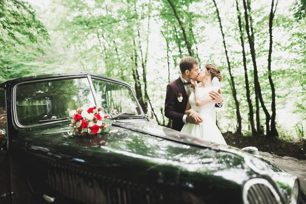 Feliz casal recém-casado, homem e mulher beijando perto de carro retro elegante — Fotografia de Stock