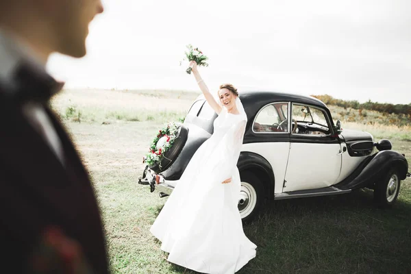 Счастливая молодожёны, муж и жена целуются возле стильного ретро-автомобиля — стоковое фото