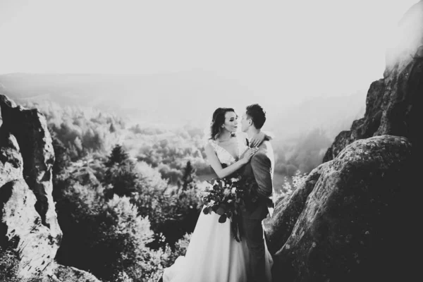 Счастливая красивая свадьба невесты и жениха в день свадьбы под открытым небом на скале гор. Счастливый брак пара на открытом воздухе на природе, мягкие солнечные огни — стоковое фото