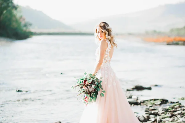 Ritratto di splendida sposa con capelli lunghi in posa con grande bouquet vicino al fiume — Foto Stock