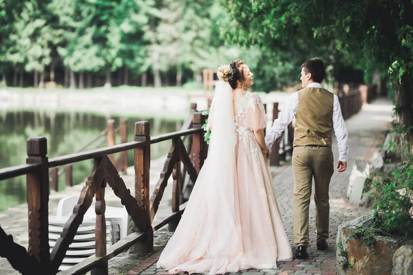 Couple élégant de jeunes mariés heureux marchant dans le parc le jour de leur mariage avec bouquet — Photo