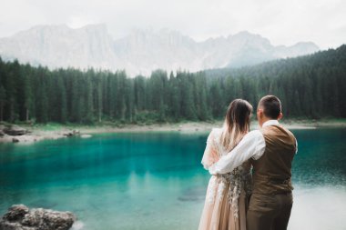 Doğadaki düğün çifti, dağlardaki güzel bir gölün yanında birbirlerine sarılıyorlar beyaz elbiseli güzel model kız. Takım elbiseli adam