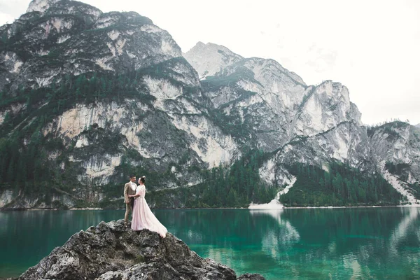 Pareja de boda en la naturaleza es abrazarse unos a otros cerca de un hermoso lago en las montañas.. Hermosa chica modelo en vestido blanco. Hombre de traje — Foto de Stock