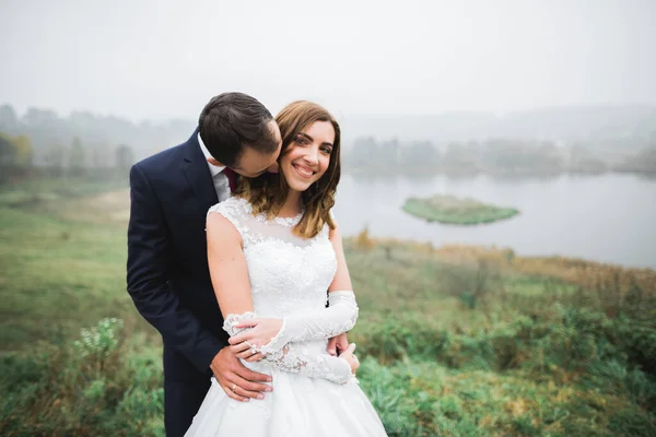 Romántico, cuento de hadas, feliz pareja recién casada abrazándose y besándose en un parque, árboles en el fondo — Foto de Stock