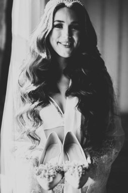 Zarif beyaz elbiseli güzel gelin ellerinde düğün ayakkabıları tutuyor.