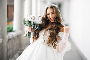 Lüks bir gelin, bir kız buketle poz veriyor ve gülümsüyor.