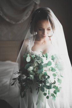 Cüppeli muhteşem gelin bir odada düğün töreni için poz veriyor ve hazırlanıyor.