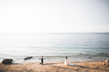 Düğün çifti mavi denizin yanındaki kayalarda öpüşüyor ve sarılıyor.