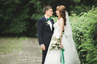 Yeni evli çiftimiz düğün günlerinde ellerinde buketle parkta yürüyorlar.