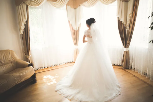 Preciosa novia en bata posando y preparándose para la ceremonia de boda cara en una habitación — Foto de Stock