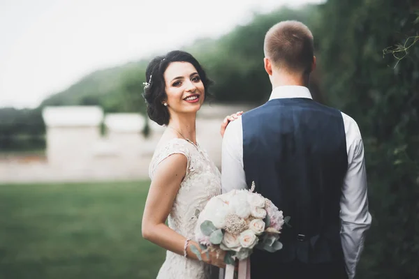 Romantic, fairytale, happy newlywed couple hugging and kissing in a park, trees in background — Stock Photo, Image