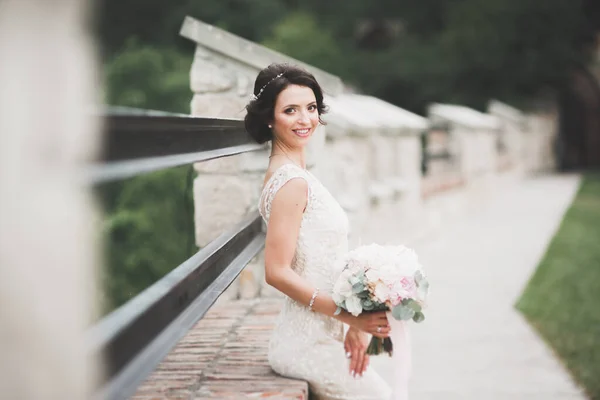 Bella sposa bruna in elegante vestito bianco che tiene bouquet in posa alberi ordinati — Foto Stock