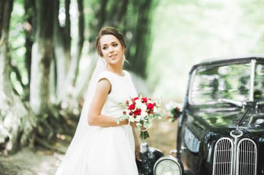 Şık, eski moda siyah arabanın yanında poz veren zarif bir gelin. Lüks ve klasik tarzda bir düğün. Portre