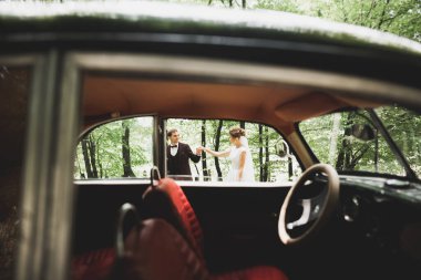 Şık bir düğün çifti, gelin, damat retro arabada öpüşüyor ve sarılıyor.