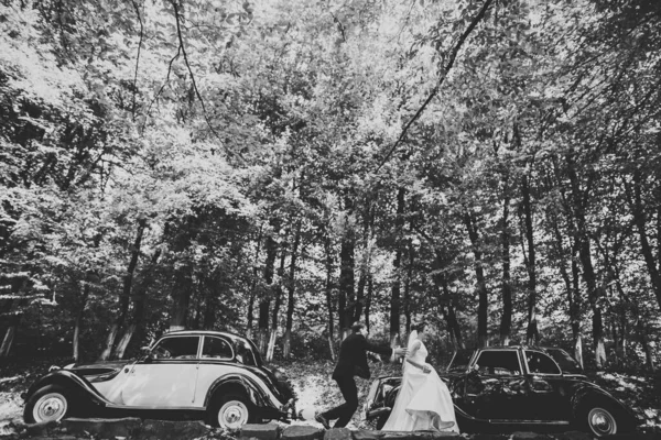 Elegante pareja de boda, novia, novio besándose y abrazándose en coche retro — Foto de Stock