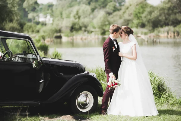 Şık bir düğün çifti, gelin, damat retro arabada öpüşüyor ve sarılıyor. — Stok fotoğraf