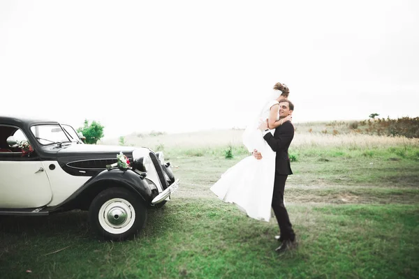 Elegante pareja de boda, novia, novio besándose y abrazándose en coche retro — Foto de Stock