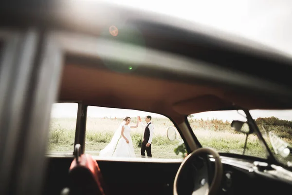 Şık bir düğün çifti, gelin, damat retro arabada öpüşüyor ve sarılıyor. — Stok fotoğraf