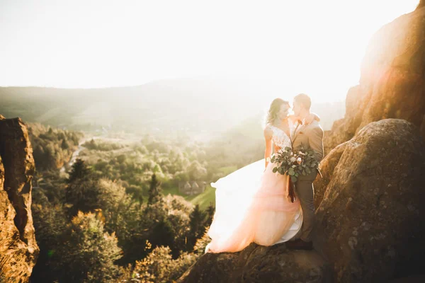 Счастливая красивая свадьба невесты и жениха в день свадьбы под открытым небом на скале гор. Счастливый брак пара на открытом воздухе на природе, мягкие солнечные огни — стоковое фото