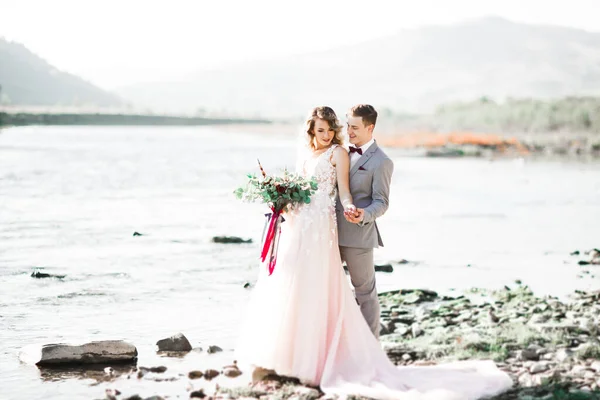 Elegante elegante sposa bionda felice e splendido sposo sullo sfondo di un bellissimo fiume in montagna — Foto Stock