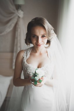 Cüppeli muhteşem gelin bir odada düğün töreni için poz veriyor ve hazırlanıyor.