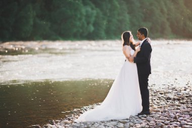 Düğün çifti, damat ve gelin kucaklaşıyor, nehir kenarında.