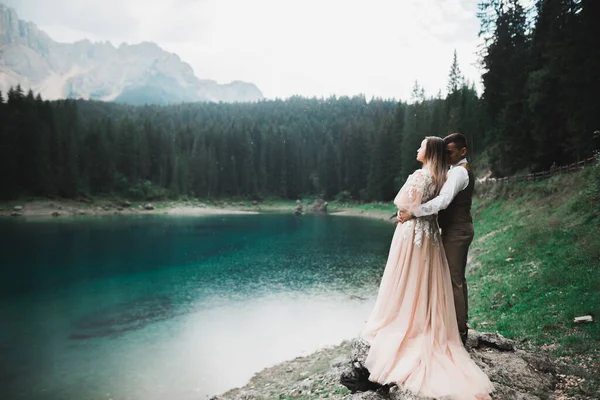 Couple de mariage sur la nature se serre dans les bras près d'un beau lac dans les montagnes.. Belle fille modèle en robe blanche. Homme en costume — Photo