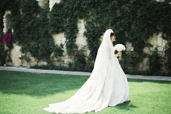 Bella sposa in elegante vestito bianco che tiene bouquet in posa nel parco — Foto Stock