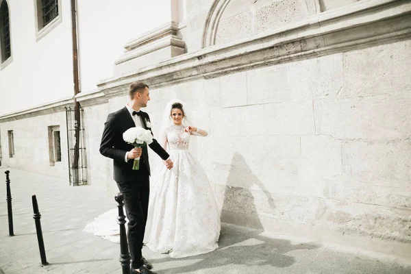 Fotografování ze svatby. Nevěsta a ženich se procházejí po městě. Manželé se objímají a dívají se jeden na druhého. Držení kytice — Stock fotografie