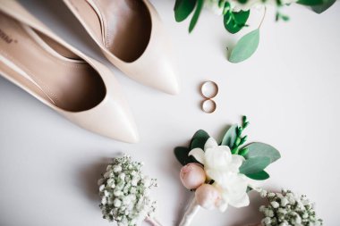 Bir çift zarif ve şık gelinlik ayakkabısı, alyansları, bir buket gülleri ve diğer çiçekleri var.