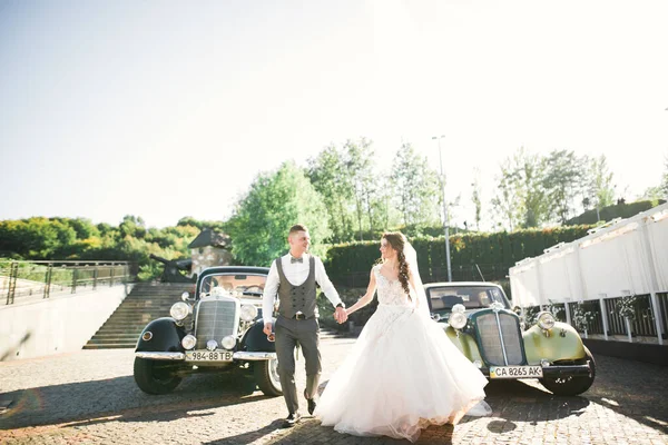 Γάμος ζευγάρι, όμορφη νύφη και κομψό γαμπρό κρατώντας τα χέρια και κοιτάζοντας ο ένας τον άλλο κοντά ρετρό γαμήλιο αυτοκίνητο — Φωτογραφία Αρχείου