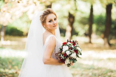 Çekici gelinin portresi, uzun saçlı, büyük buketli poz veren.