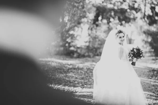Elegante pareja de recién casados felices caminando en el parque el día de su boda con ramo — Foto de Stock