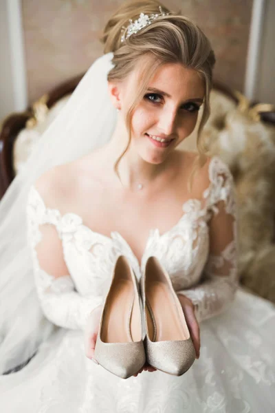 Hermosa novia de lujo en elegante vestido blanco sostiene zapatos de boda en las manos —  Fotos de Stock