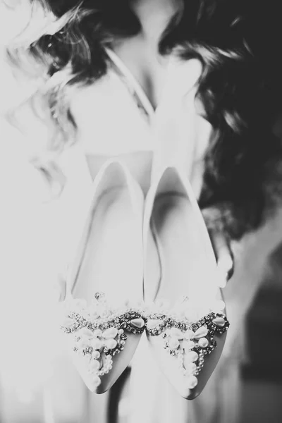 우아 한 흰색 드레스를 입은 아름다운 호화 로운 신부가 결혼용 신발을 손에 쥐고 있다 — 스톡 사진